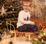 Living kidney recipient Joseph sitting in front of a Christmas tree. He is facing away to the right but is turning towards the camera, a large grin on his face.