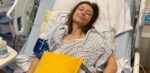 Living kidney donor Julie lying in a hospital bed. She is dressed in a hospital gown with her head laying against the pillow, and is smiling at the camera